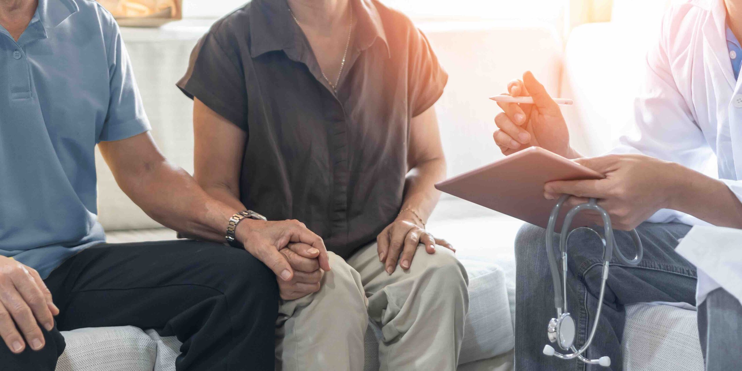 Elderly couple holding hands while talking to doctor.